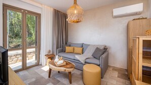 Een moderne woonkamer met een grijze bank, een houten bijzettafeltje, een rond hocker en een hanglamp.