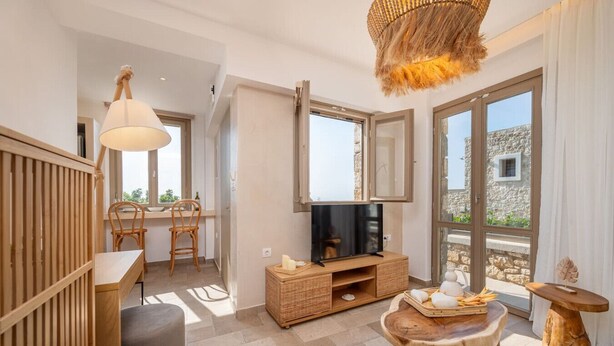 Een moderne woonkamer met een televisie, houten meubels en grote ramen met uitzicht op de omgeving.