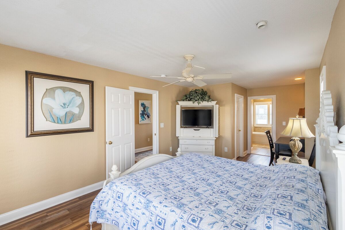 A bedroom with a bed, a television, a desk with a lamp, and a ceiling fan.