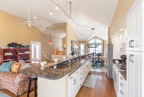 A spacious kitchen with a central island, white cabinetry, and pendant lighting. - Pet-friendly semi oceanfront home w/ pool and hot tub by Sun Realty (Nags Head)