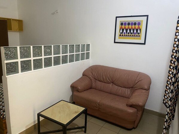 Une pièce avec un canapé en cuir marron, une petite table, un rideau à motifs et une œuvre d’art encadrée accrochée au mur.