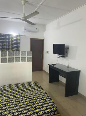 Une chambre à coucher comprenant un lit, un bureau, un téléviseur et un ventilateur de plafond.