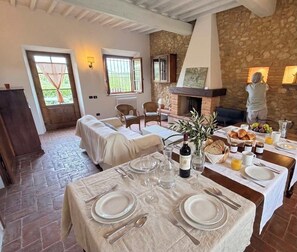 A dining area with a stone wall, a fireplace, and a table set for breakfast with plates, cutlery, and a bottle of wine. - Podere Casanova Ruber - View of San Gimignano (San Gimignano)