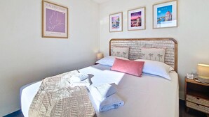Ein ordentlich bezogenes Bett mit Handtüchern, ein Kopfteil mit Palmenmuster und drei gerahmte Bilder an der Wand.