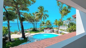 Une piscine avec vue sur la mer, entourée de palmiers et bordée d’un bâtiment blanc.