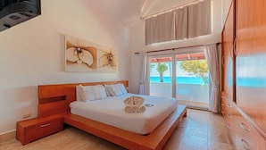 Une chambre avec un lit en bois, une table de chevet, une grande fenêtre avec des rideaux et une vue sur la mer.