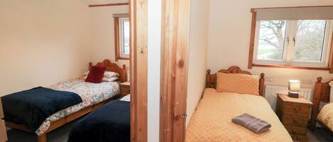 A bedroom with two single beds, wooden headboards, a nightstand with a lamp, and a window providing natural light.