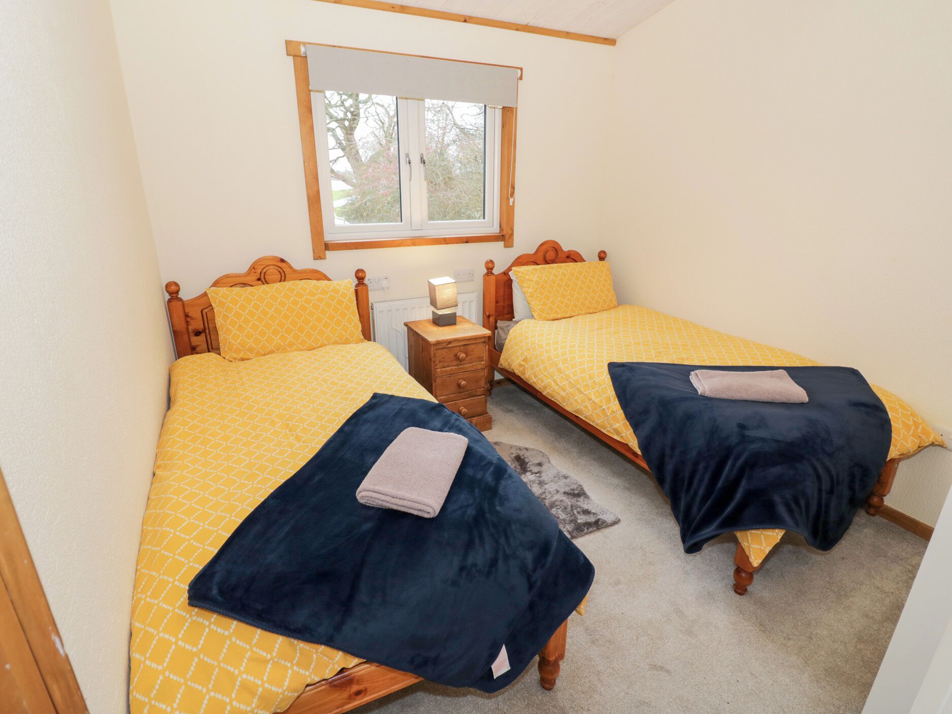 Una habitación con dos camas individuales, cada una con cabecero de madera, una mesita de noche y una ventana sobre las camas.