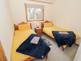 Una habitación con dos camas individuales, cada una con cabecero de madera, una mesita de noche y una ventana sobre las camas.