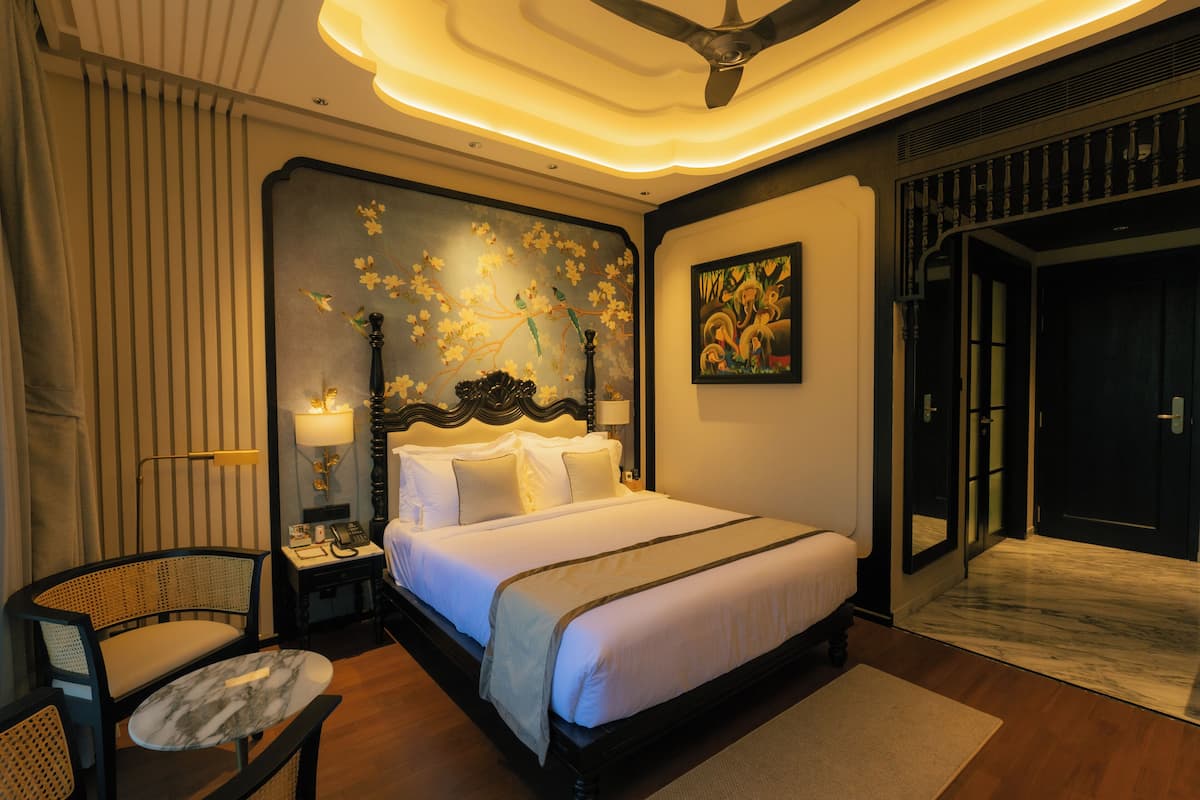 Une chambre d’hôtel avec un grand lit, un bureau avec une lampe, une chaise et un ventilateur de plafond.