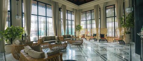 A spacious lobby with a high ceiling, large windows, and a polished marble floor.
