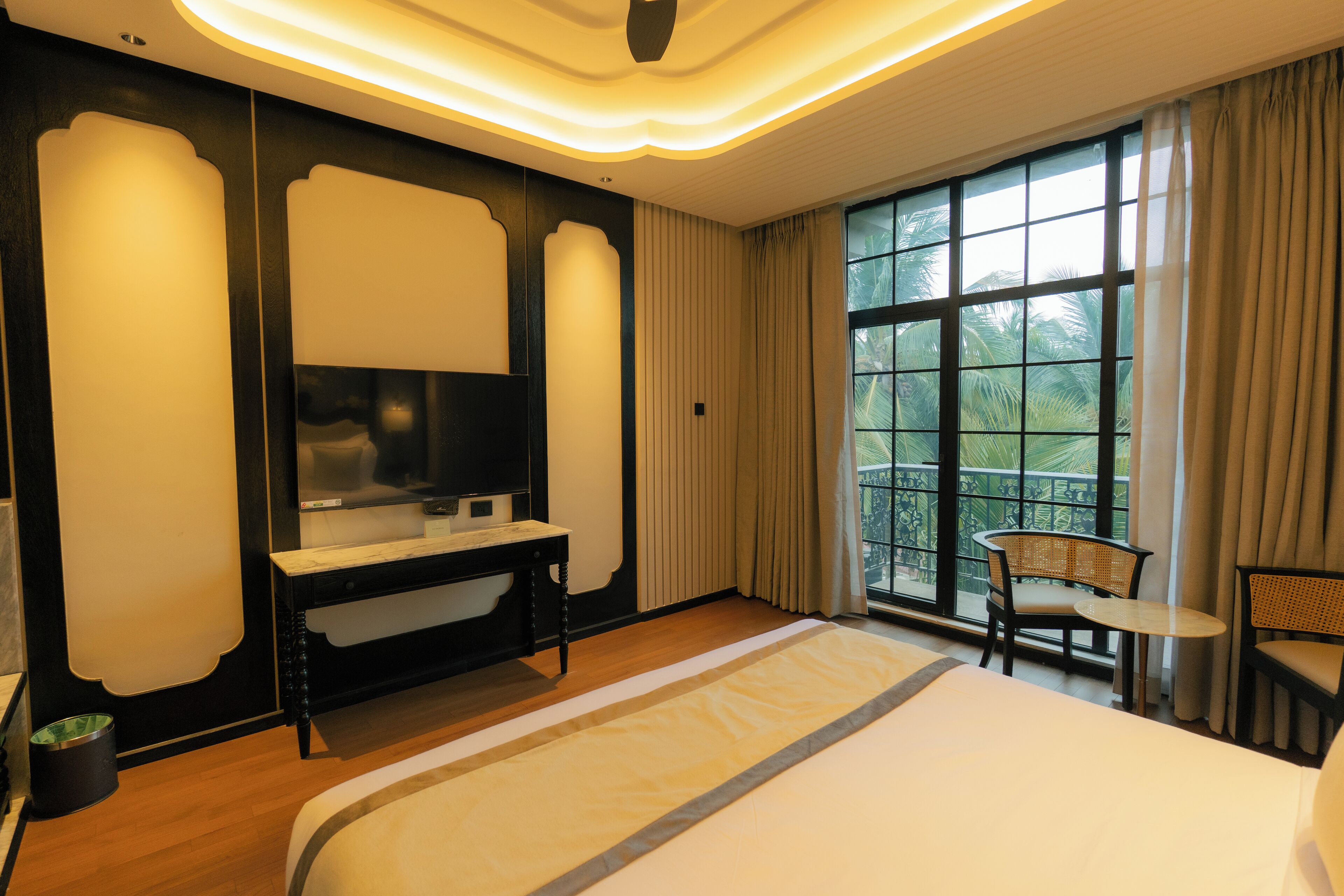 Habitación de hotel con una cama grande, televisión, escritorio y vista a palmeras por la ventana.