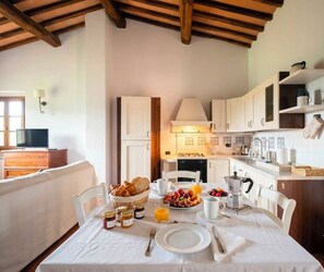 A breakfast table set with croissants, fruit, and coffee in a kitchen with white cabinets and a wooden ceiling. - Podere Casanova - Caesius Home Pool & View (San Gimignano)