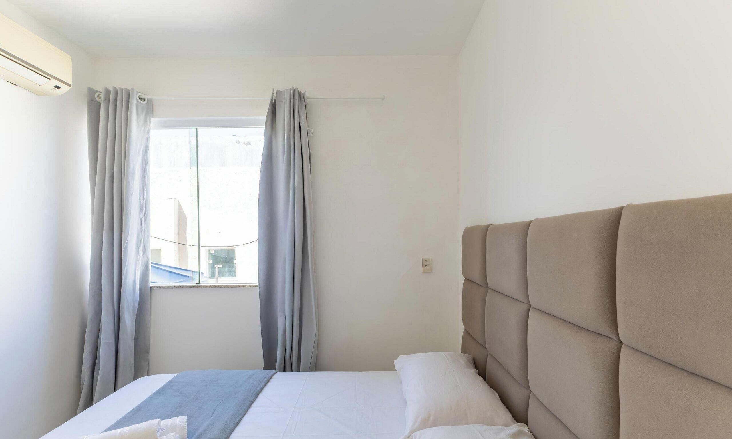 A hotel room with a bed, a window with curtains, and a wall-mounted air conditioner.