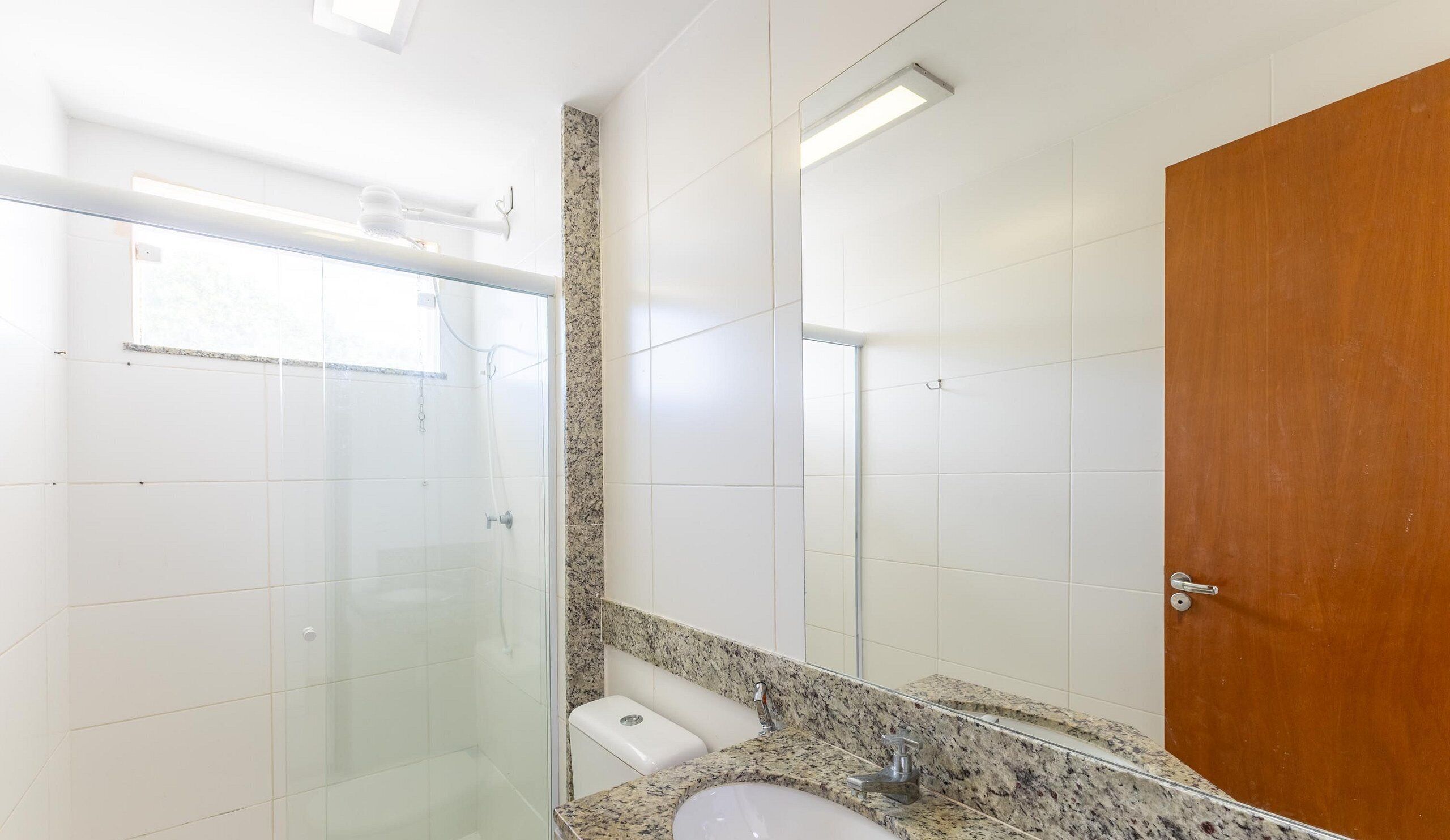 A bathroom with a glass shower enclosure, a sink with a granite countertop, and a wooden door.