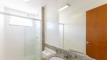 A bathroom with a glass shower enclosure, a sink with a granite countertop, and a wooden door.