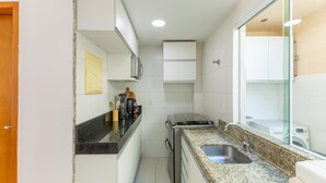 Een kleine keuken met witte kastjes, een granieten aanrecht, een ingebouwde kookplaat en een spoelbak.
