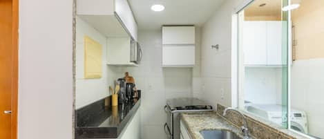 A compact kitchen with white cabinets, a granite countertop, a built-in stove, and a sink.