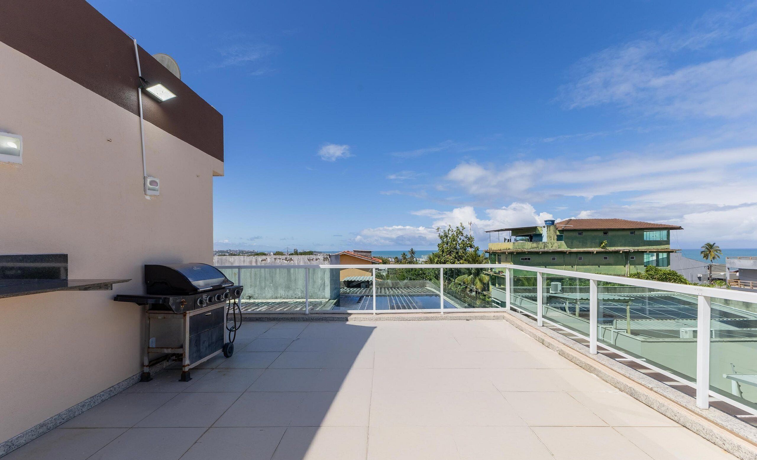 A rooftop terrace with a barbecue grill, a pool, and a view of the sea and buildings.