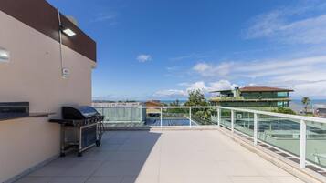 A rooftop terrace with a barbecue grill, a pool, and a view of the sea and buildings.