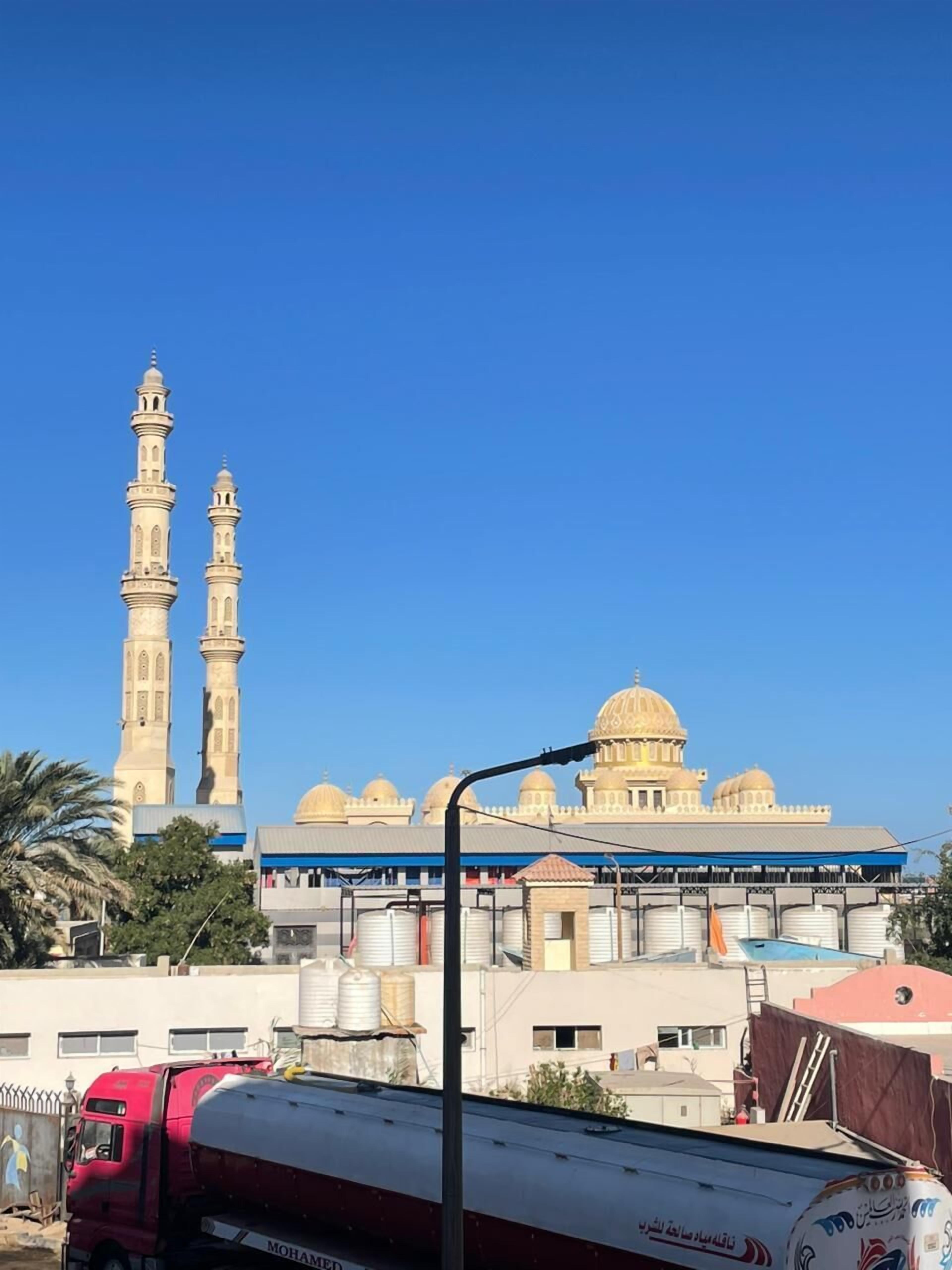 Una mezquita con dos minaretes y una cúpula grande, rodeada de edificios residenciales y una camioneta roja.