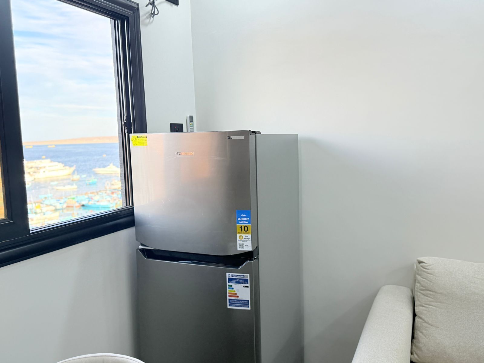 A stainless steel refrigerator in a room with a window overlooking a harbor.