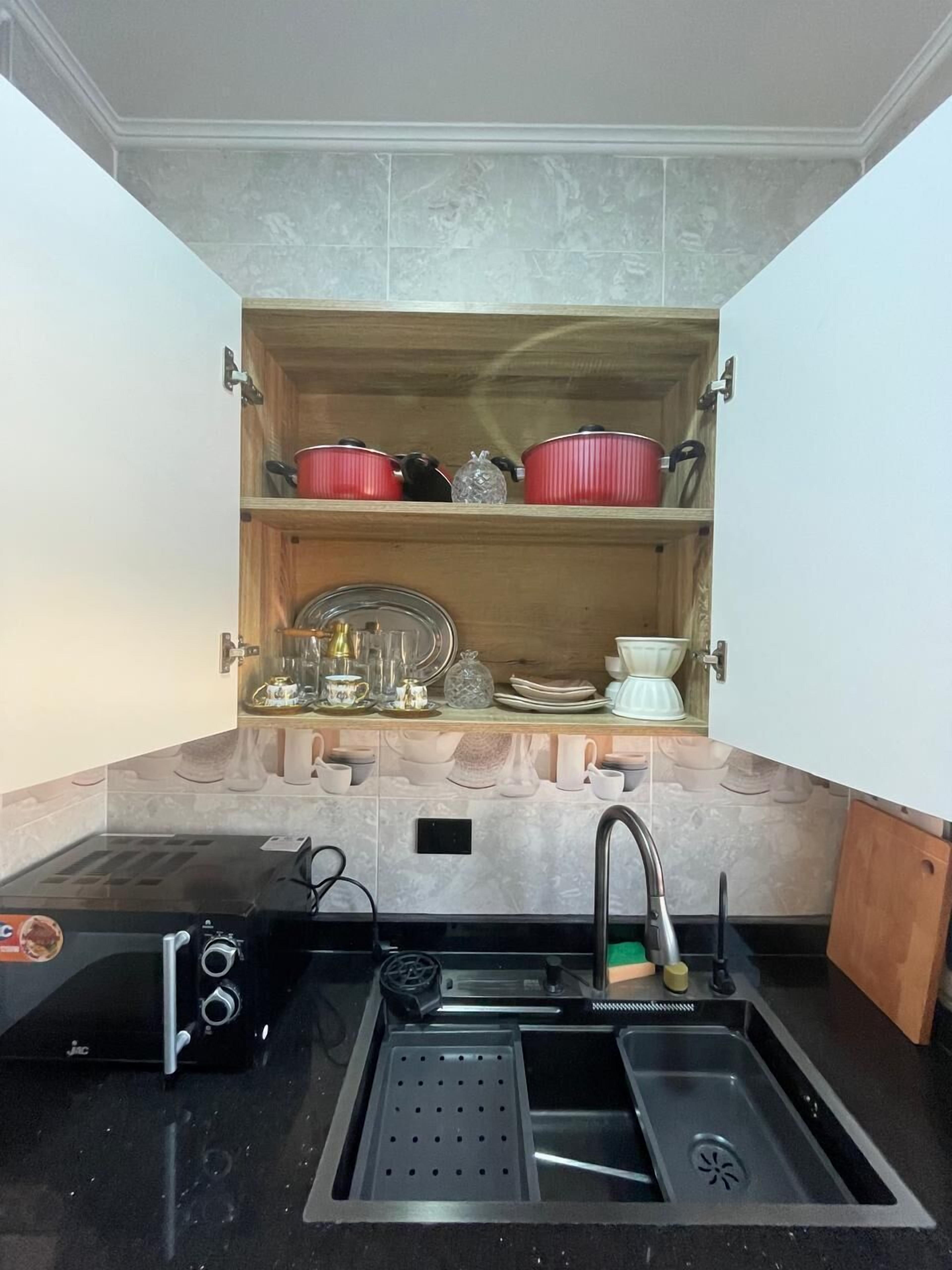 A kitchen with a built-in shelf above the sink holding various kitchenware.