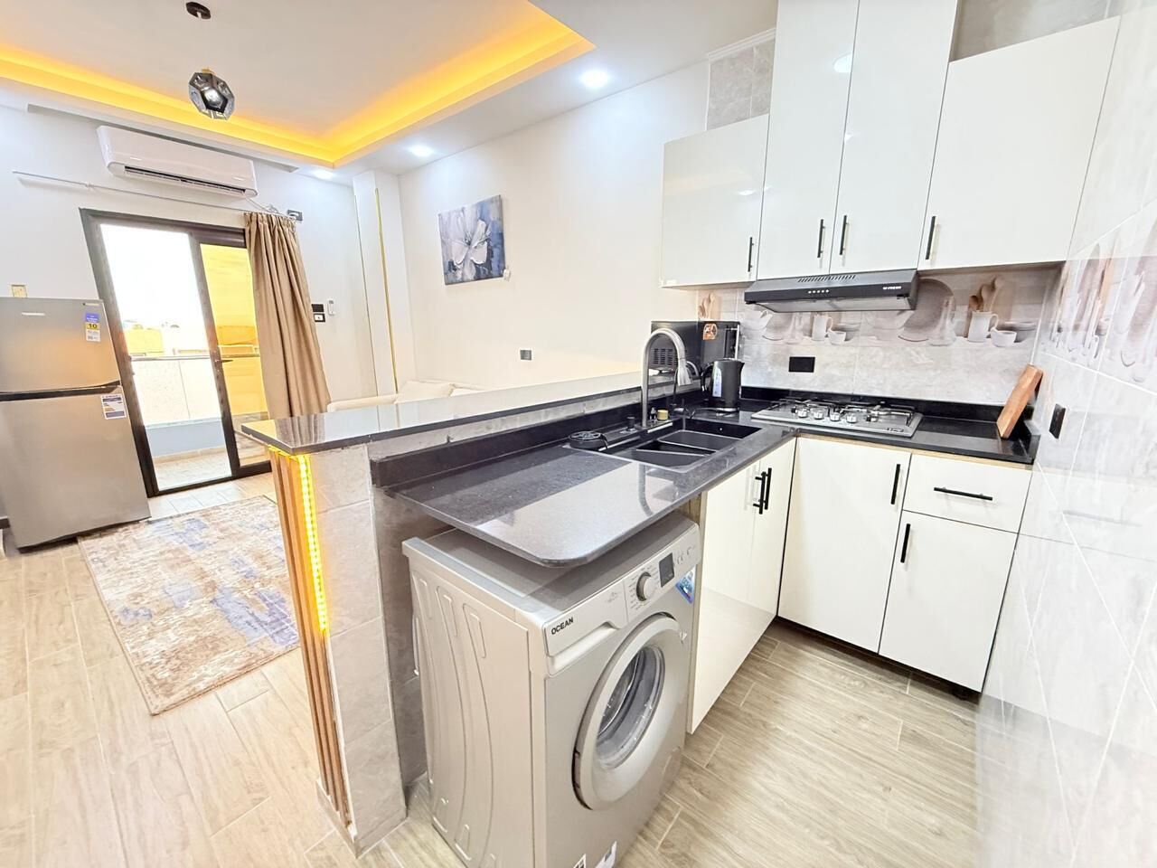 A modern kitchen with a built-in washer and dryer, white cabinets, and a large island with a sink.