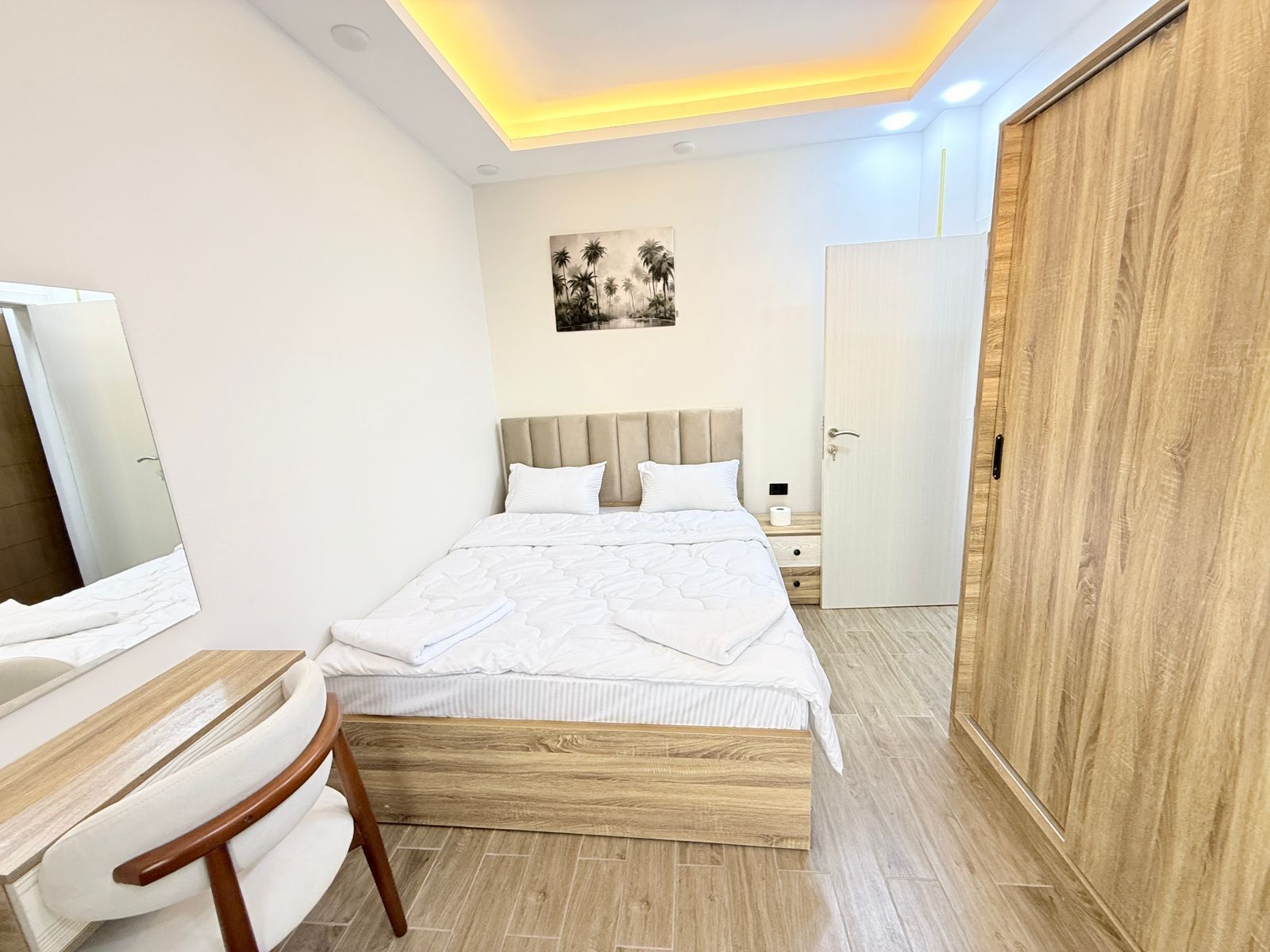 Ein modernes Schlafzimmer mit Bett, Nachttisch, Sessel, Kleiderschrank und einem Bild an der Wand.