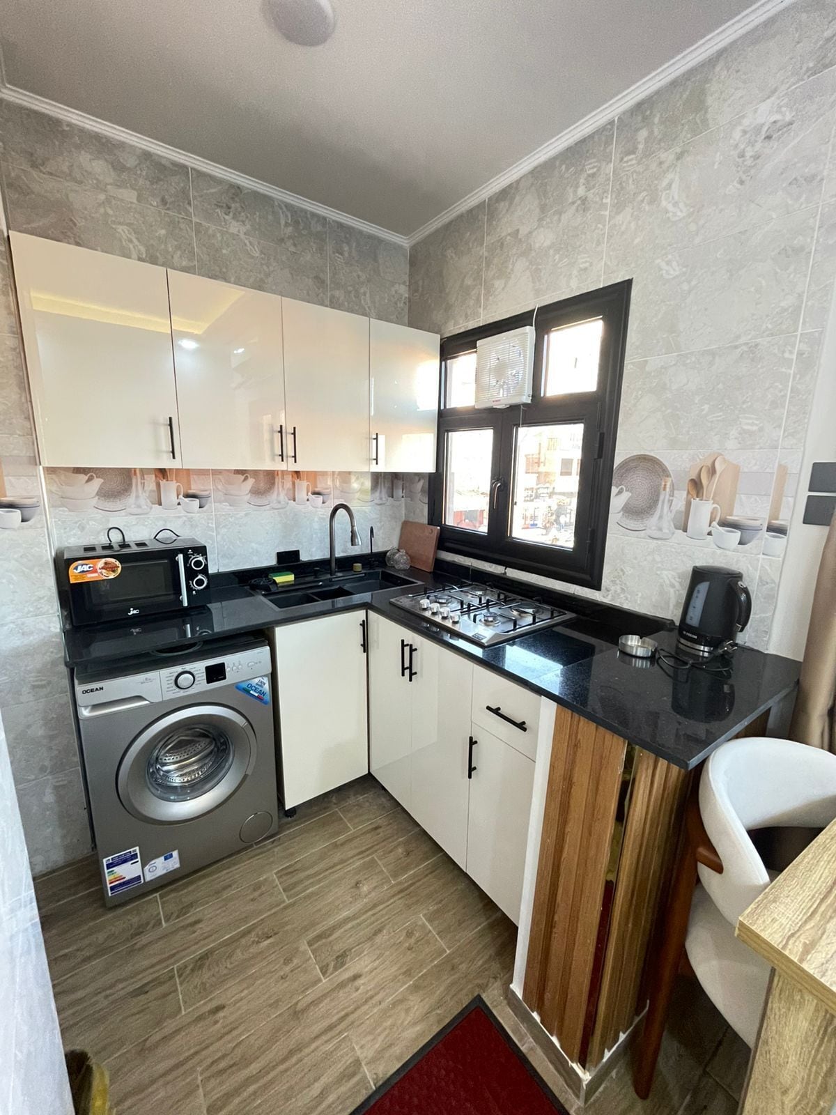 Cocina compacta con lavadora y secadora integradas, estufa y ventana con vistas.