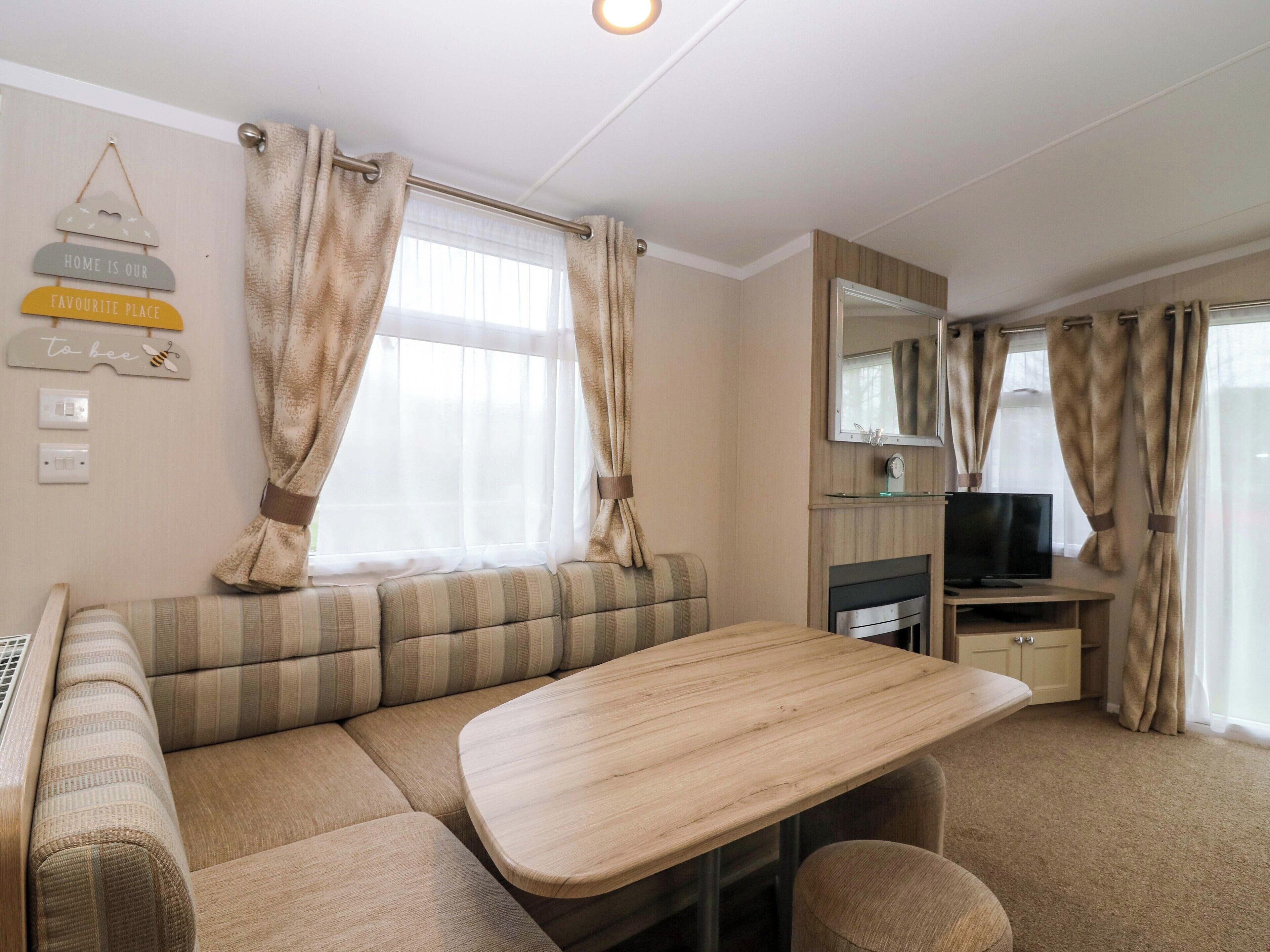 A cozy RV interior with a sofa, a dining table, a TV, and curtains.