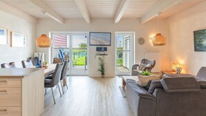 A spacious living area with a dining table, sofa, and a television mounted on the wall. - skandinavisches Reihenhaus in Dagbüll (Dagebüll)