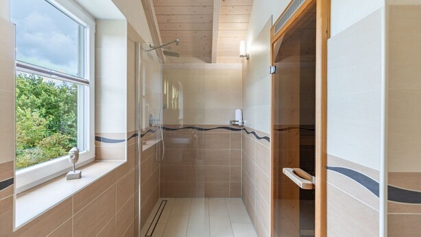 A modern bathroom with a shower, a window, and a view of greenery outside. - skandinavisches Reihenhaus in Dagbüll (Dagebüll)