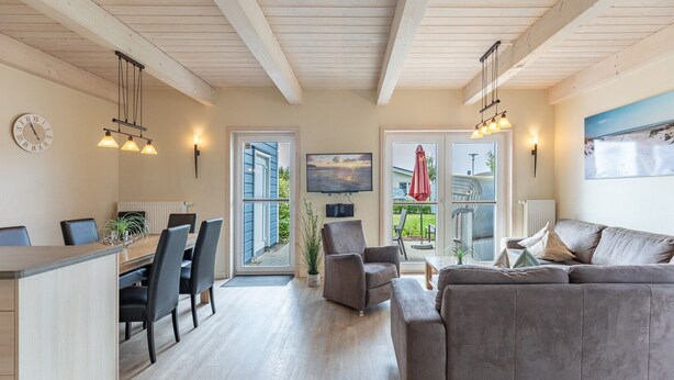 Una sala de estar moderna con un sofá gris, un comedor con una mesa y sillas de madera, y una zona de cocina con mostrador y sillas.
