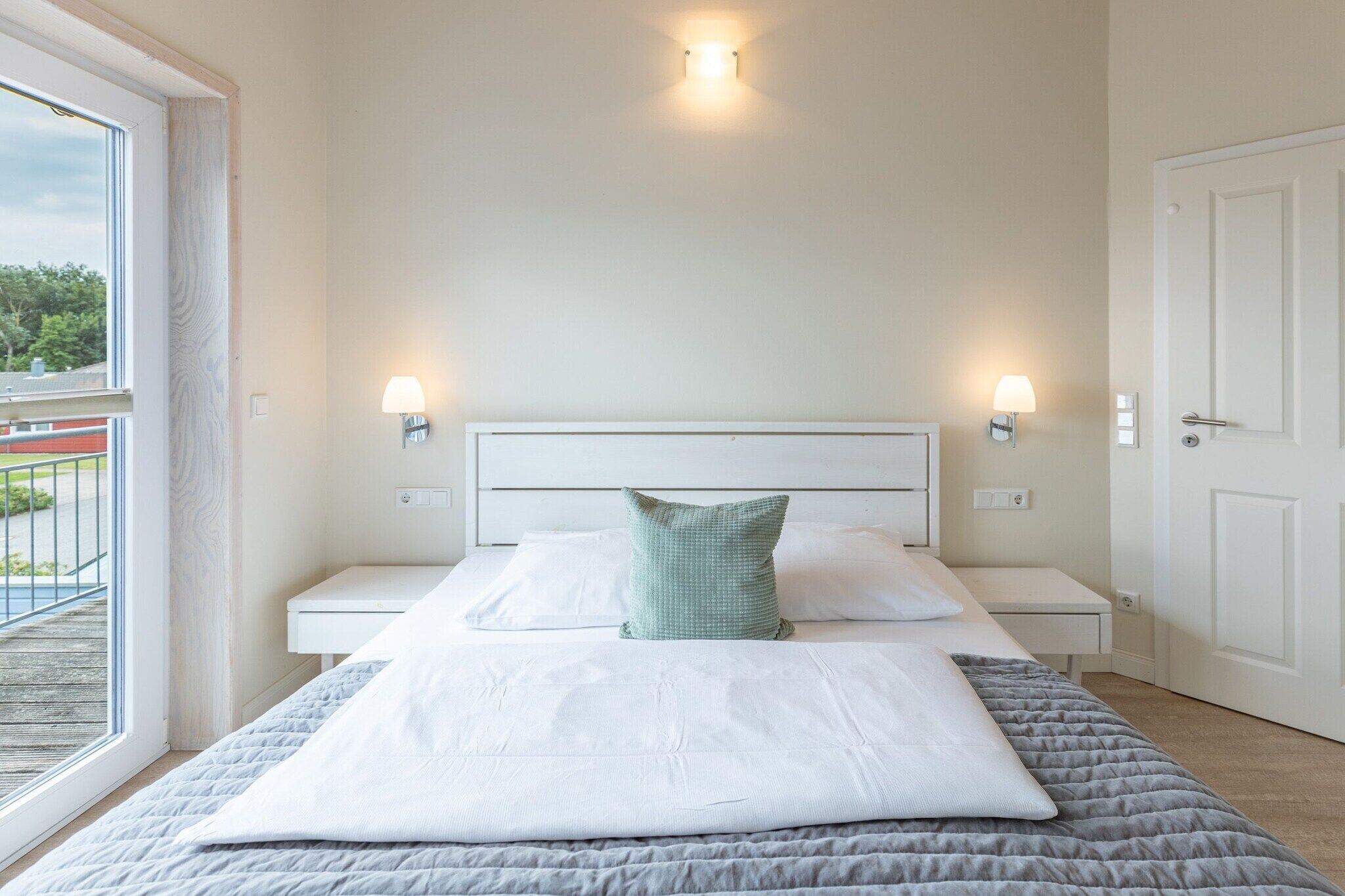 A bedroom with a bed, two bedside tables, a nightstand, a window with a view, and a door.