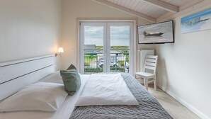 Un dormitorio con cama, una silla, un televisor y un balcón con vistas.