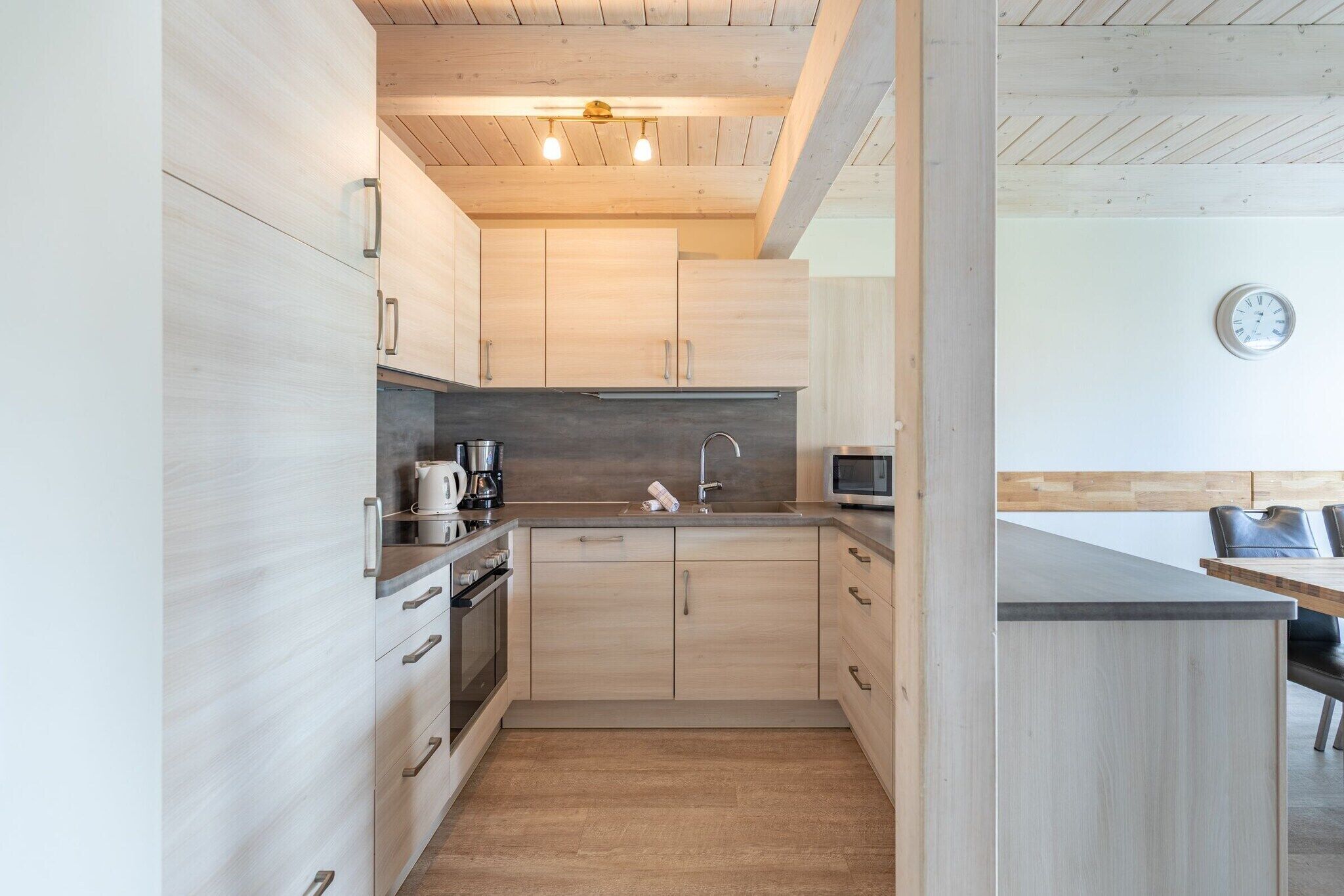 Eine moderne Küche mit hellen Holzschränken, Edelstahlgeräten und einer Holzzieldecke.