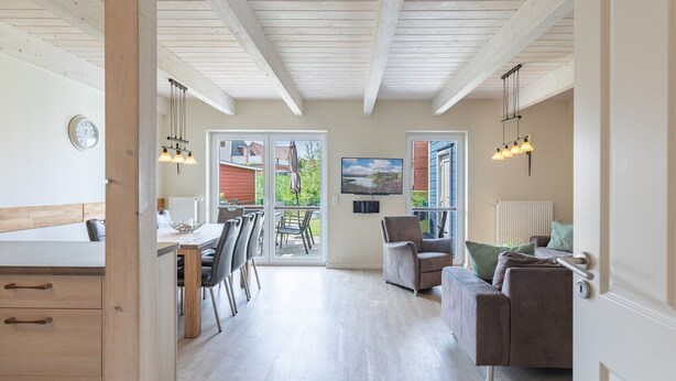A spacious living area with a dining table, chairs, a sofa, and a TV. There is a large window with a view of the outdoors. - skandinavisches Reihenhaus in Dagbuell mit Sauna (Dagebüll)