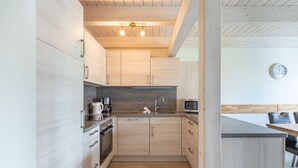 A modern kitchen with light wood cabinets, stainless steel appliances, and a wooden ceiling. - skandinavisches Reihenhaus in Dagbuell mit Sauna (Dagebüll)