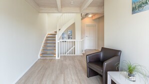 A staircase leading to a second floor, a dark leather chair, a small table with a plant, and a door in the background. - skandinavisches Reihenhaus in Dagbuell mit Sauna (Dagebüll)
