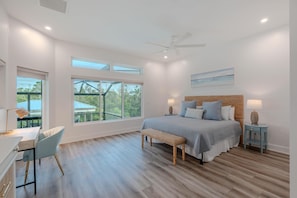 Quarto com uma cama grande, uma escrivaninha e uma cadeira. Há janelas e um ventilador de teto.