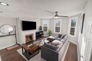 A living room with a fireplace, sofa, television, and a ceiling fan. - Stylish Modern 3BR 2BA Family Retreat - Deck + Private Parking (Pittsburgh)