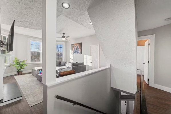 A modern interior with a staircase, a living area with a sofa and a painting, and a kitchen area with a TV. - Stylish Modern 3BR 2BA Family Retreat - Deck + Private Parking (Pittsburgh)