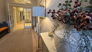 Een gang met een lamp, een vaas met gedroogde takken en een deur die naar een andere kamer leidt.