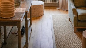 Een gezellige woonkamer met een groot raam, een radiator, een bank, een tafel met lampen en een vloerkleed.