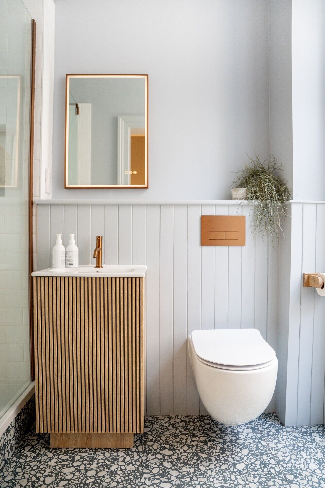 Een badkamer met een houten wastafelmeubel, een wit toilet, een spiegel en een potplant.