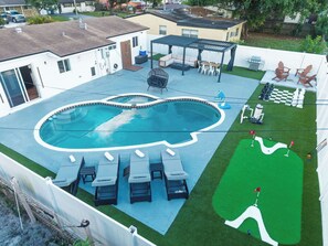 A backyard with a swimming pool, lounge chairs, a barbecue area, and a miniature golf course.