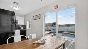 A modern kitchen with white cabinets, a black refrigerator, and a dining area with a wooden table and white chairs. - Private Pool, Giant Chess, Golf, Games  by Ventur (Hollywood)