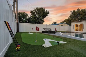 A backyard with artificial grass, a pool, and a flag.