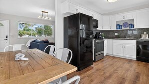 A modern kitchen with white cabinets, a black refrigerator, and a dining area with a wooden table and chairs. - Private Pool, Giant Chess, Golf, Games  by Ventur (Hollywood)